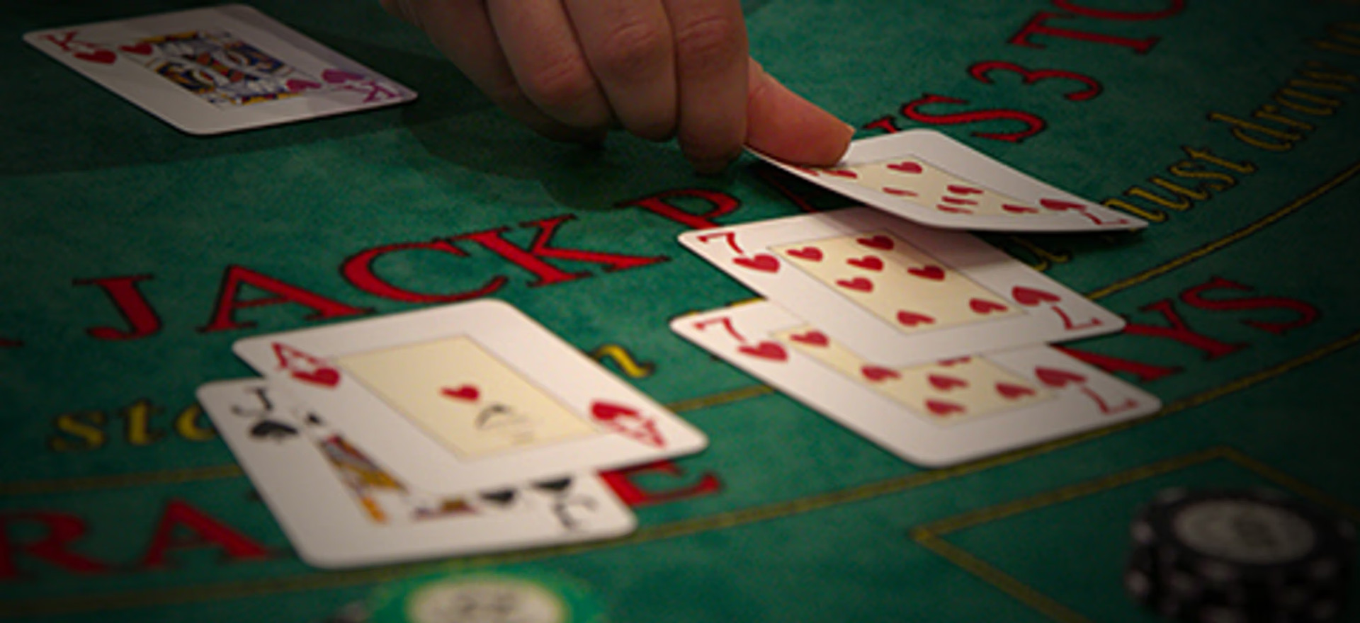 Hånd der tager et kort på et blackjack-bord med kort og jetoner.