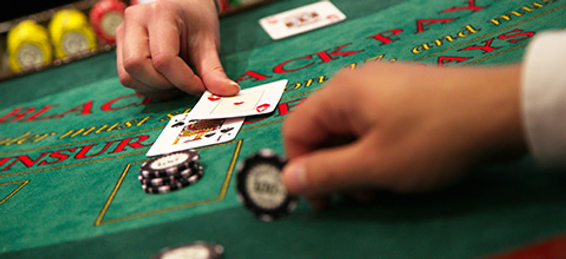 Hænder, kort og jetoner på et blackjack-bord.