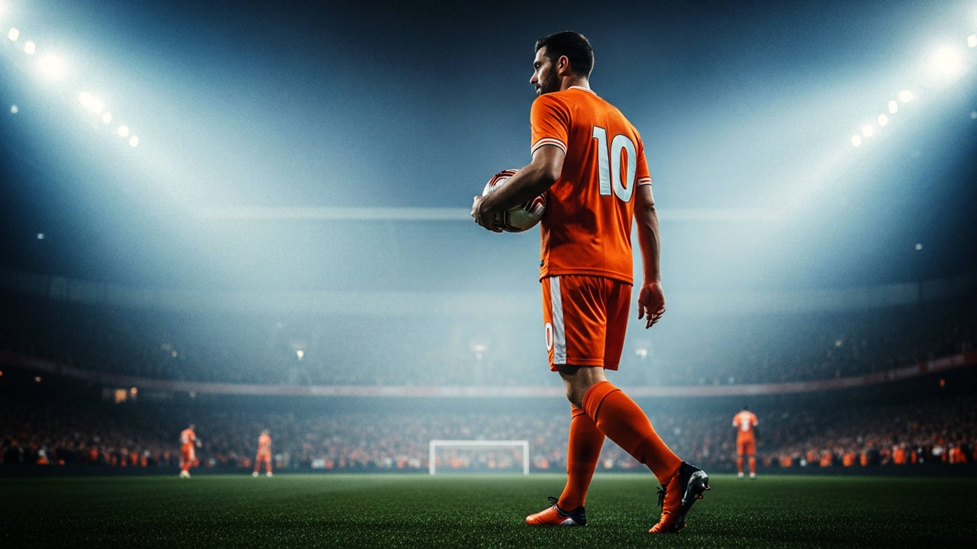 Fodboldspiller i orange trøje med nummer 10 går med bolden i hånden på banen i et oplyst stadion med tilskuere i baggrunden.