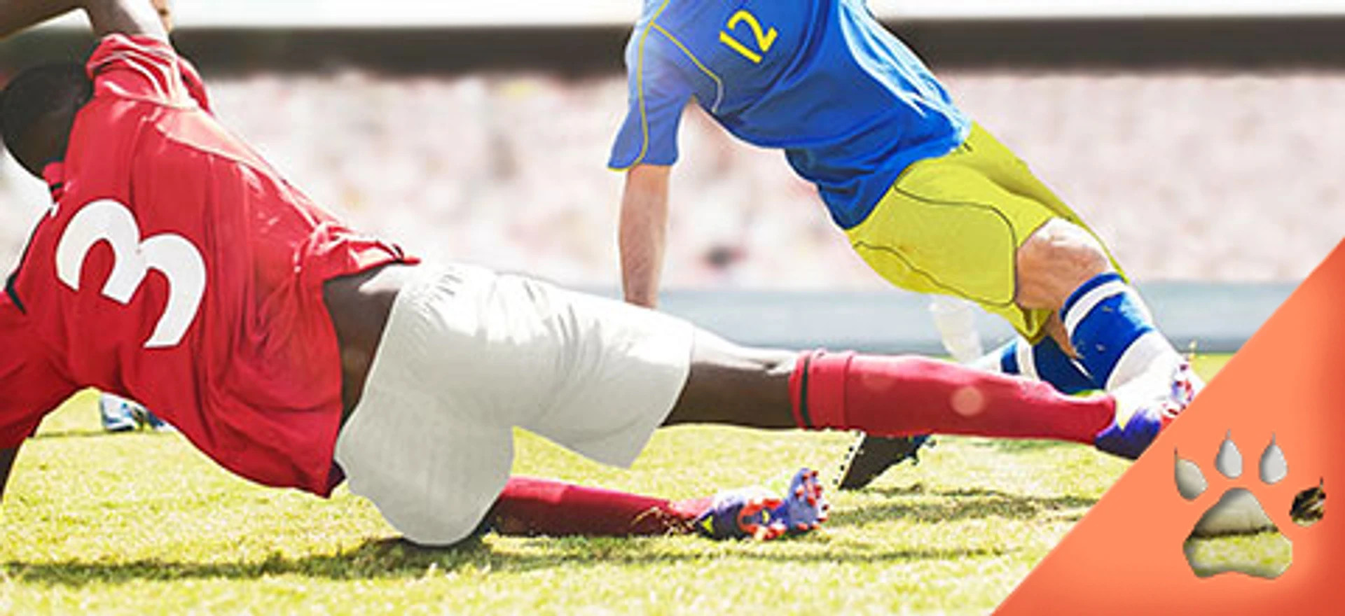 To fodboldspillere i glidende tackling under en kamp på græsplæne