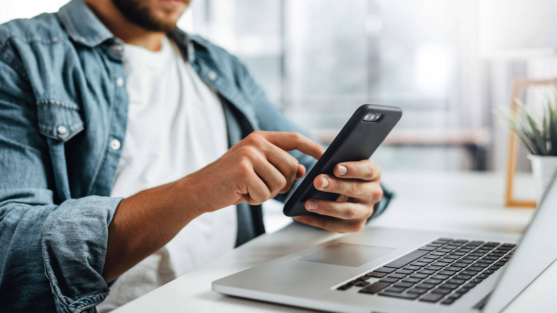 Person bruger smartphone ved laptop i hjemmemiljø